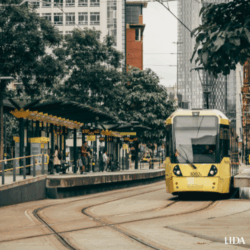 Tram at a city centre stop in Manchester, UK with pedestrians waiting to board.